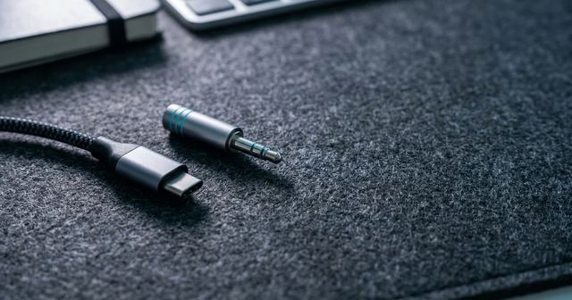Portátil plateado conectado a auriculares sobre una mesa blanca de trabajo